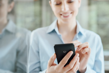 Woman using a smartphone and leaning on a window