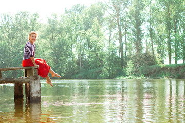 Fototapeta na wymiar pretty young woman in red dress sitting on pier