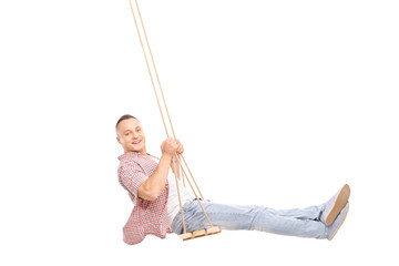 Delighted young man swinging on a wooden swing