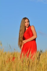 Obraz premium Young beautiful woman and a red dress in a wheat field