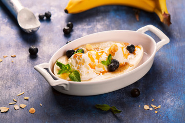 Delicious banana split with blueberry, mint, almonds and sauce on blue wooden background. Selective focus