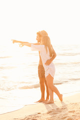 Sunset, sandy beach, a loving couple walks embraced on the deserted beach at sunset during a day at the beach on vacation. The loving couple shows something with his hands in the sea