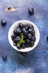 Fototapeta na wymiar Fresh organic blueberry in white bowl on blue grunge wooden background. Top view