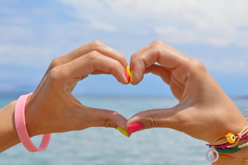 Heart shape made of hands against sea and sky