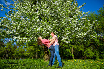 a man and woman hug under the crown of flowering tree