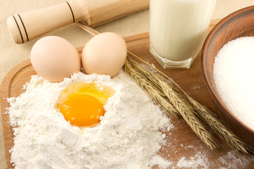 Still life of bread, eggs, cereals, flour and kitchen tools on a wooden board