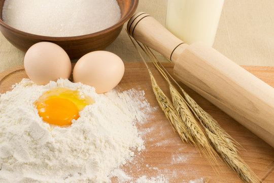 Still life of bread, eggs, cereals, flour and kitchen tools on a wooden board