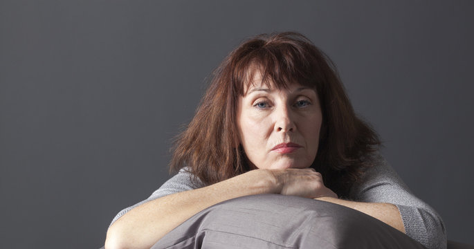overwhelmed mature woman resting her face and hands laying down on cushions for comfort while being sick or depressed
