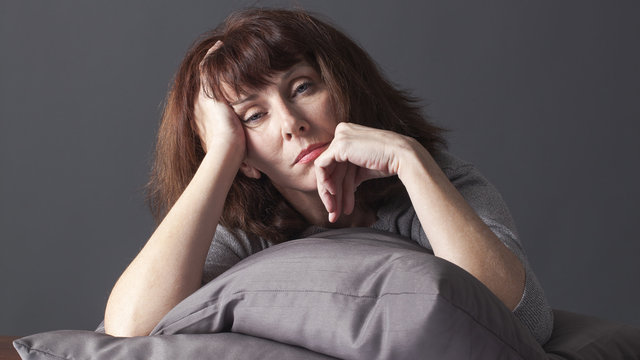sick mature woman resting her face and hands laying down on cushions for comfort while having health care problems