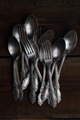 Stack of silver forks and spoons on wooden background.