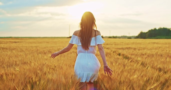 Beautiful girl running on sunlit wheat field. Slow motion 120 fps. Sun lens flare. Freedom concept. Happy woman having fun outdoors in a wheat field on sunset or sunrise. Slow motion. Harvest.