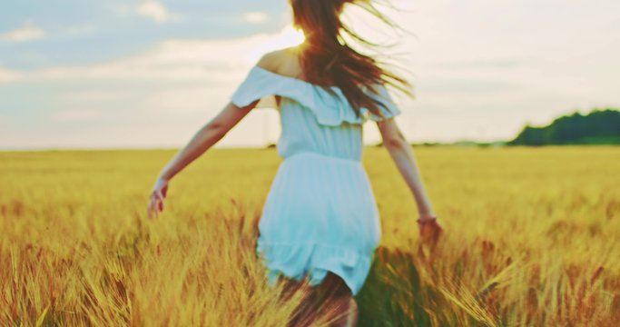 Beautiful girl running on sunlit wheat field. Slow motion 120 fps. Sun lens flare. Freedom concept. Happy woman having fun outdoors in a wheat field on sunset or sunrise. Slow motion. Harvest.