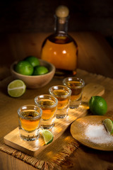 Tequila shots grouped together with a bottle and cut limes on a restaurant bar table
