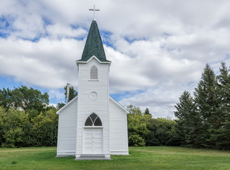 quaint little country church sitting in a green meadow surrounded by trees in the summer time