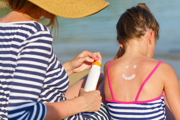 Mother applying sunscreen to her daughter at the beach