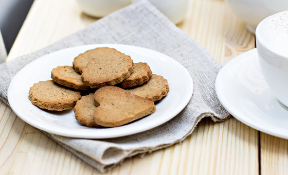 Ginger biscuits, cinnamon, a cup of hot coffee. Walnuts, hazelnuts on a wooden background