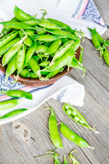 young green peas in the pod, earthenware dish, rustic background