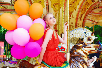 Fototapeta na wymiar Lifestyle concept, happy young woman with colorful latex balloons in the amusement park riding a carousel