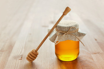 Natural honey in a pot or jar with twine tied in a bow and honey dipper on a wooden background
