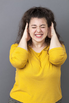 young xxl girl wearing yellow putting hands on ears to avoid hearing oversized questions, ignoring someone, not wanting to hear their side of story or having painful headache