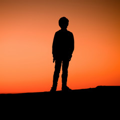 Young boy is standing on pier enjoying the sunset. Silhouette of