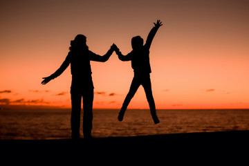 Silhouette of young mother having fun with her son, sunset