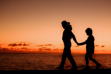 Fototapeta na wymiar Silhouette of a young mother and her son walking along a pier in