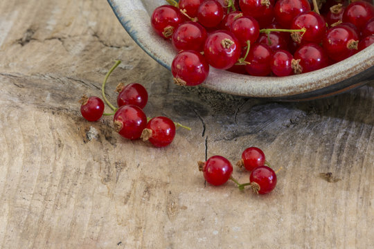 red currants falling out of a ceramic bowl on rustic wood