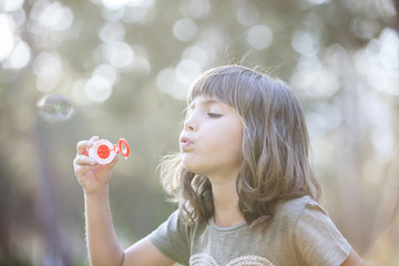 Little girl blowing soap bubbles outdoor at sunset - happy carefree childhood