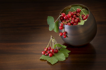 red currants with leaves in a bowl, dark brown background with c