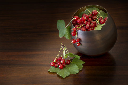 red currants with leaves in a bowl, dark brown background with c