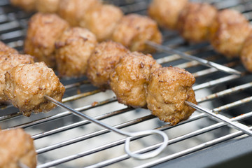 BBQ Meatballs - Meatballs on metal skewers being grilled on a barbecue.
