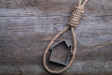 Small house framed with hangman's noose on brown wooden surface - obrazy, fototapety, plakaty