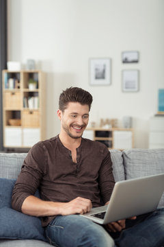 lächelnder mann mit laptop auf dem sofa
