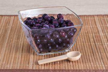 Frozen blueberry in a glass bowl with a wooden spoon