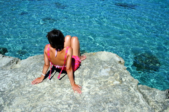 Woman sitting on the rocks by sea, Salento, Puglia, Italy