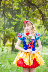 Portrait of a beautiful young blonde woman in a suit of Snow White. The girl is holding a red rose. Soft focus