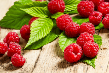 Fresh ripe raspberries with large leaves on the old wooden table