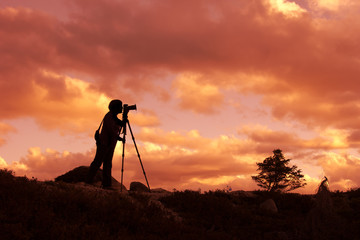Silhouette of photographer taking photo in sunset on mountain top