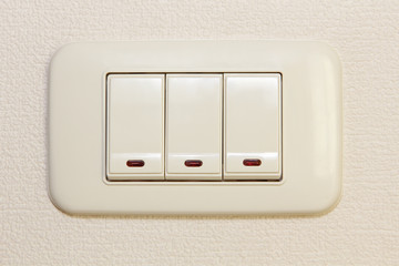 Threefold multiply light switch on beige wall.