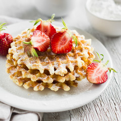 waffles with strawberries on a white plate on a light surface