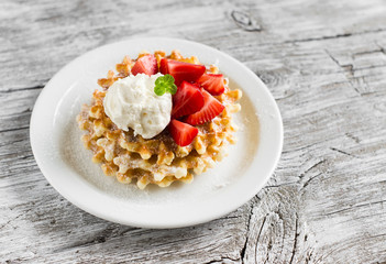 waffles with vanilla ice cream and strawberries on a white plate on a light wooden background