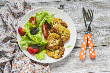 fritters of zucchini and fresh vegetable salad on a light wooden background