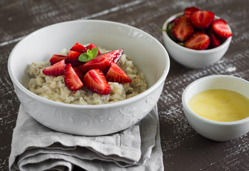 oatmeal with strawberries in a white bowl and orange juice on a dark wooden background