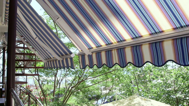 Terrace of hotel with retractable striped awning overlooking seaside