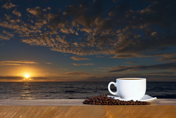 coffee cup on wood table at sunset or sunrise beach
