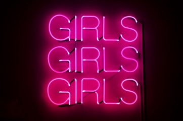 Girls Girls Girls sign glows in racy pink neon against dark night background - 86296914