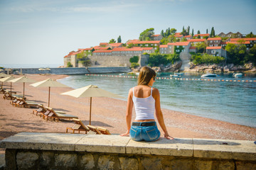 Fototapeta na wymiar Beautiful young woman looking at the seascape and island Sveti Stefan. Montenegro, Europe.