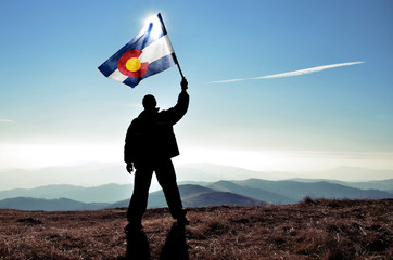 successfull silhouette man winner waving Colorado flag on top of the mountain peak