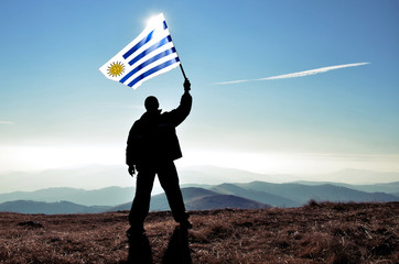 successfull silhouette man winner waving Uruguay flag on top of the mountain peak